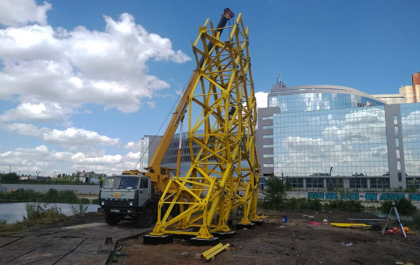 Yellow tower construction with crane and truck in front of a glass building.