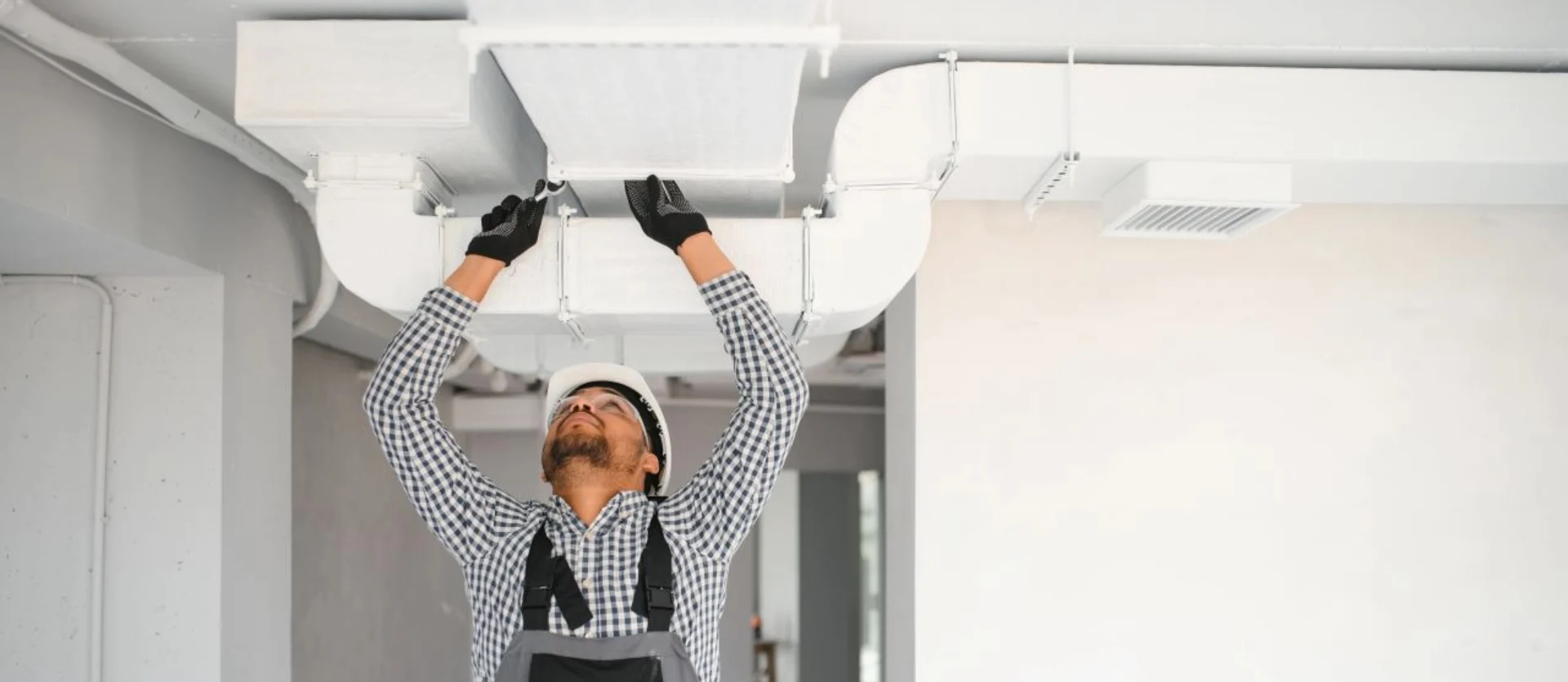 Worker in overalls installing ceiling ventilation system in a modern interior space