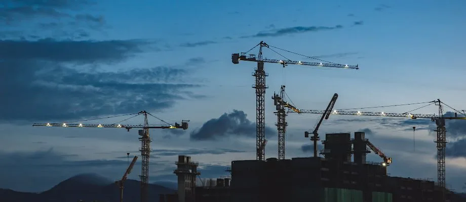 A silhouette of a construction site with multiple cranes against a twilight sky.