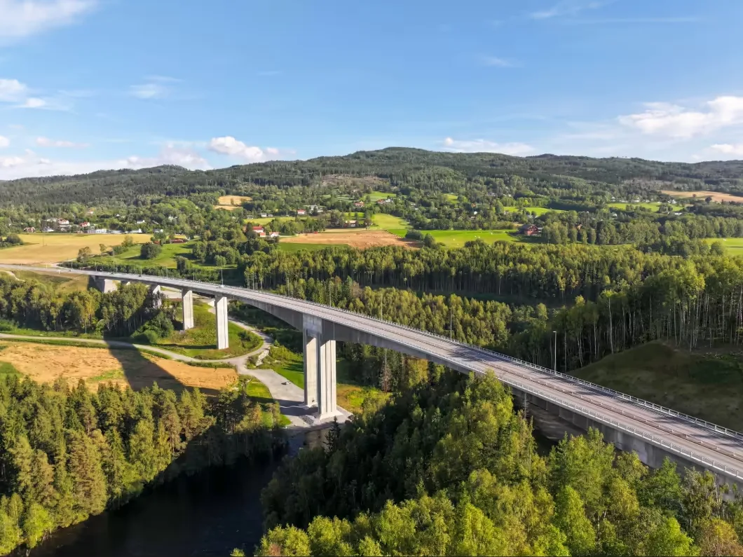 Randselva Bridge, made of modern concrete with multiple support pillars arcs over a river and forest.