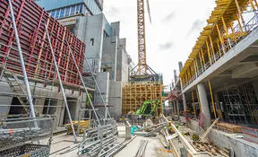 Construction site with heavy machinery, scaffolding, and unfinished concrete structures.
