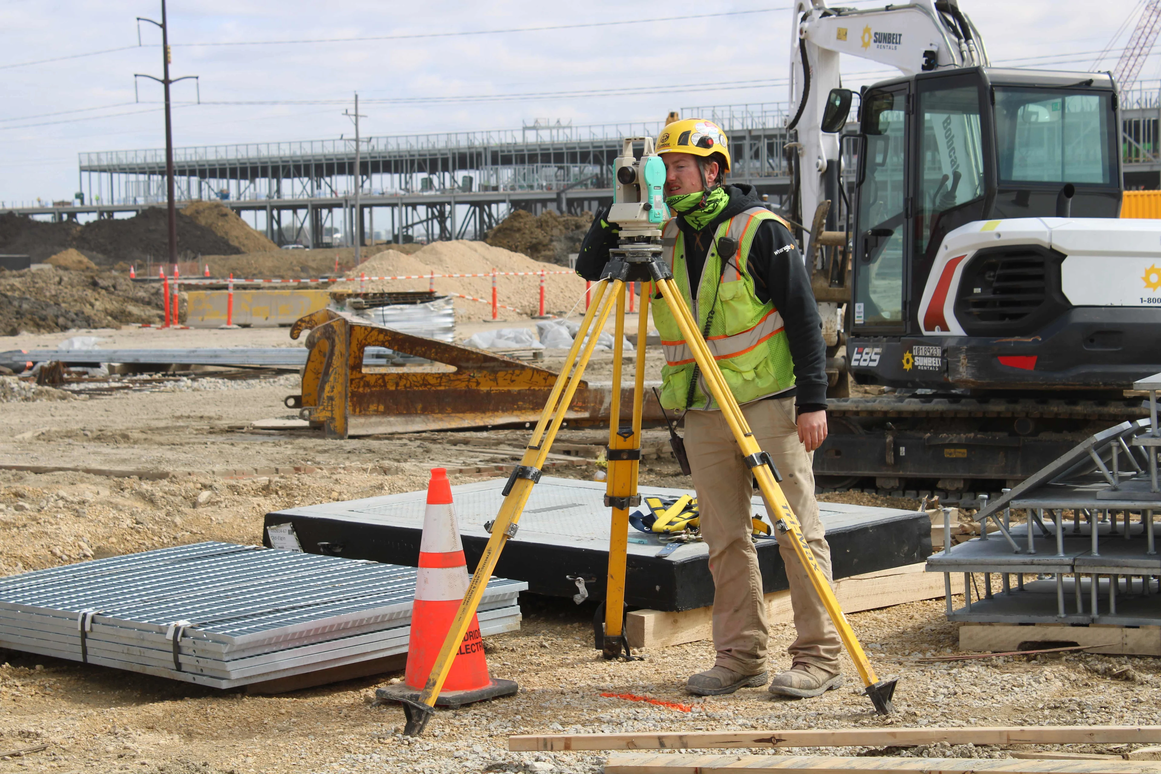 Surveyor using a total station with a construction site in the background.