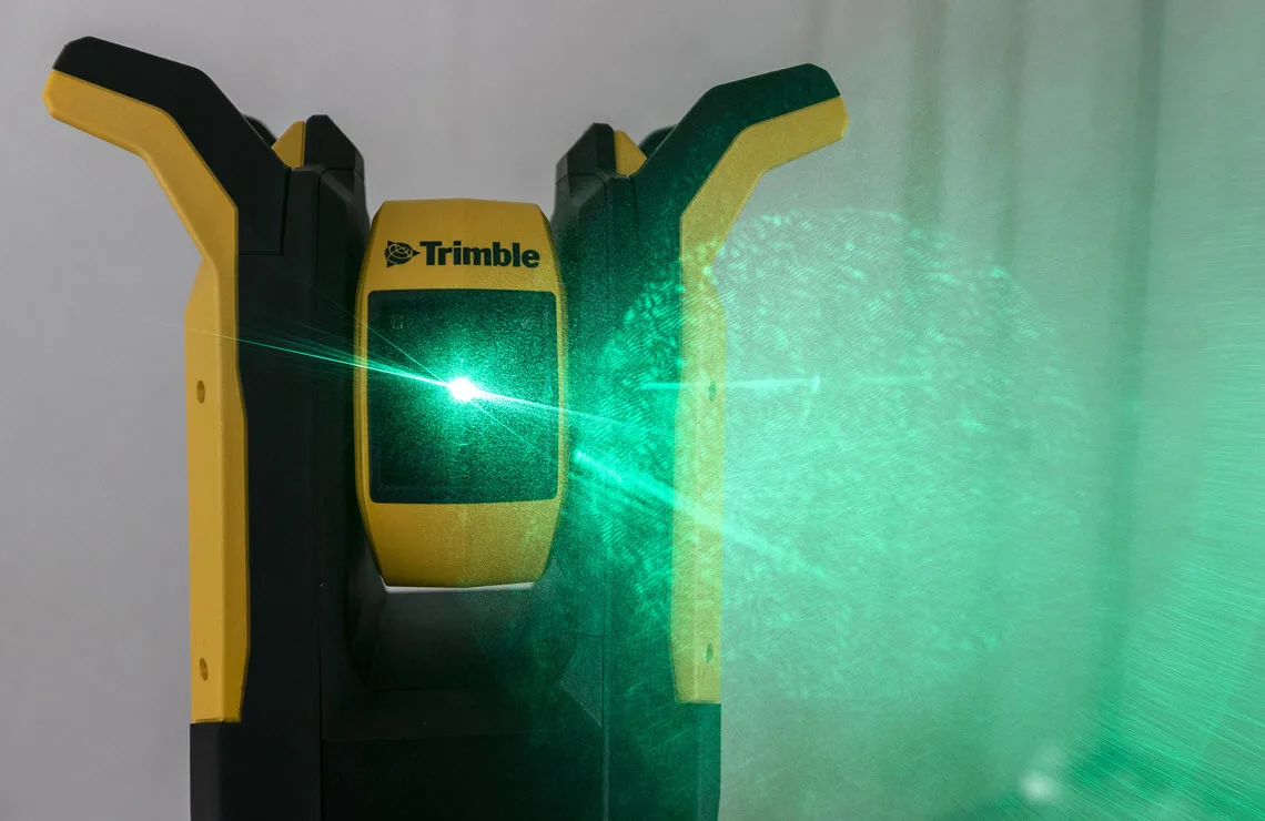 Trimble laser level projecting a bright green laser line across a wall.