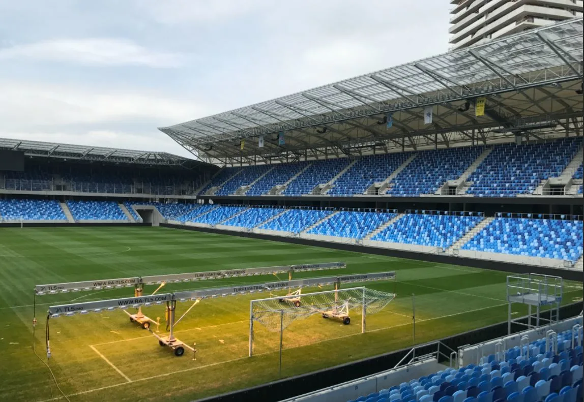 Empty stadium with blue seating and portable lights on the field.