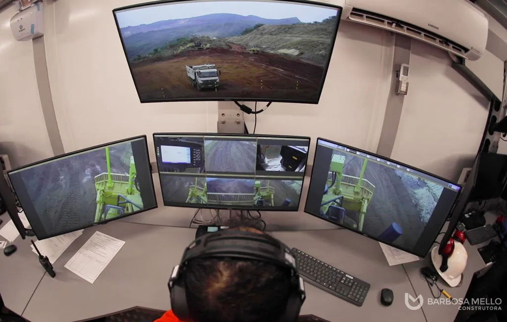 Mine operations control room with multiple monitors showing drone footage and equipment feeds.