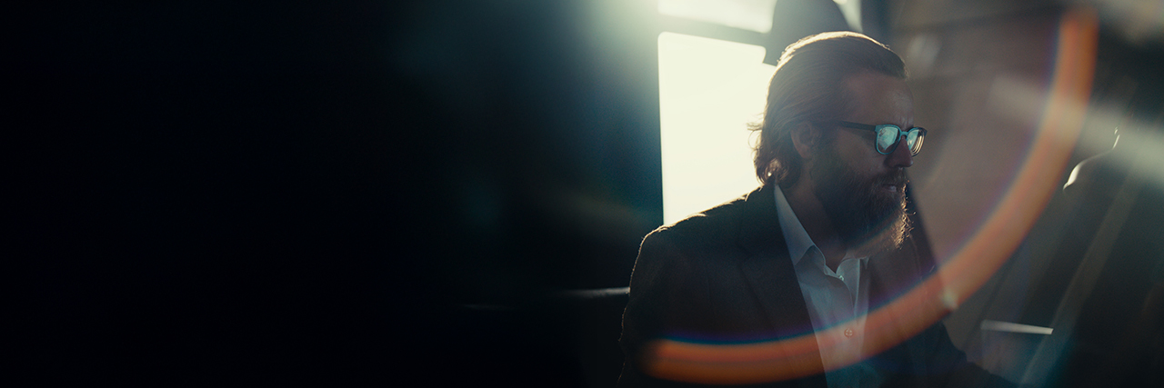 Joseph Fulco, with brushed back brown hair and glasses and backlit by a window, focuses on his screen.