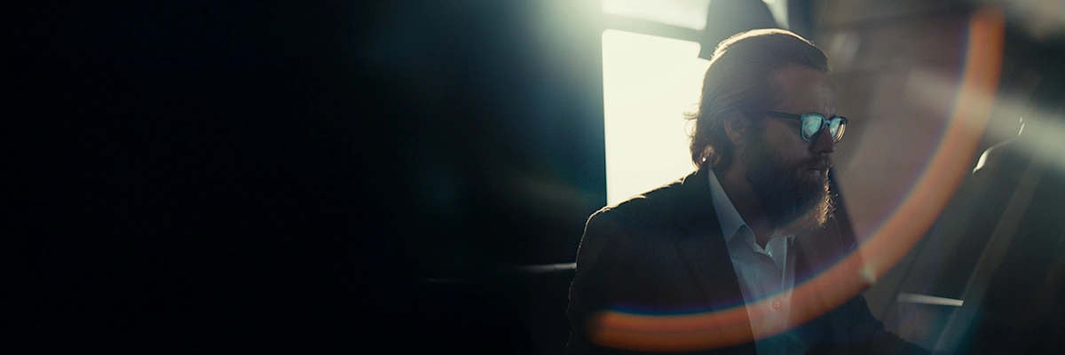 Joseph Fulco, with brushed back brown hair and glasses and backlit by a window, focuses on his screen.