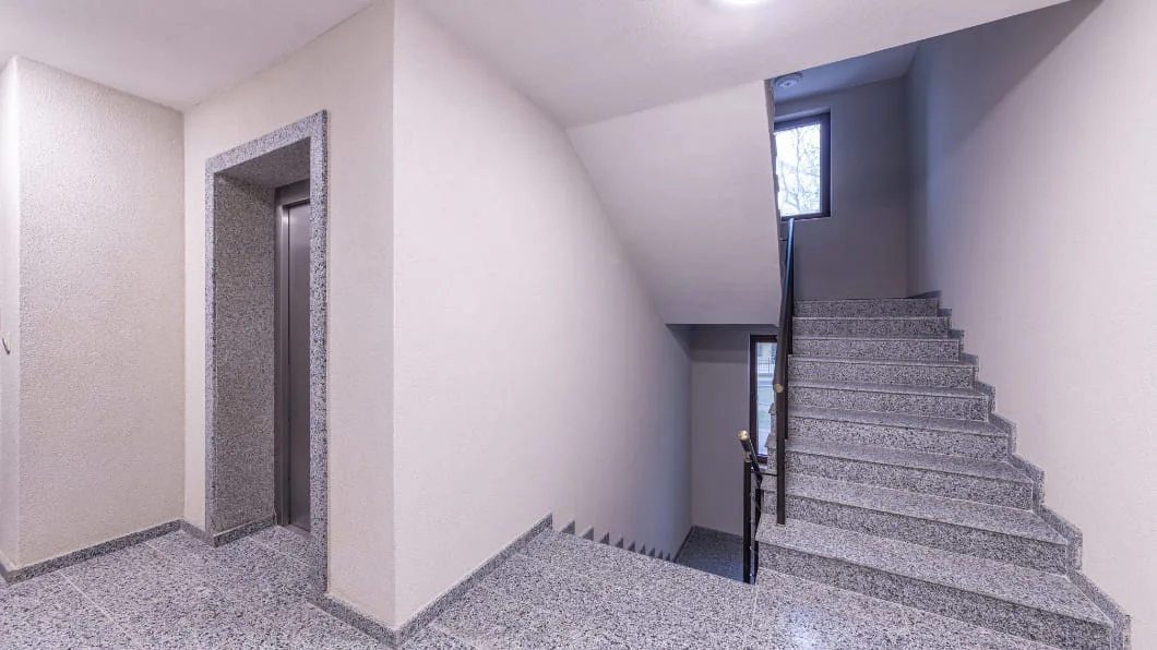 A clean, modern building interior featuring a granite staircase next to an elevator entrance.