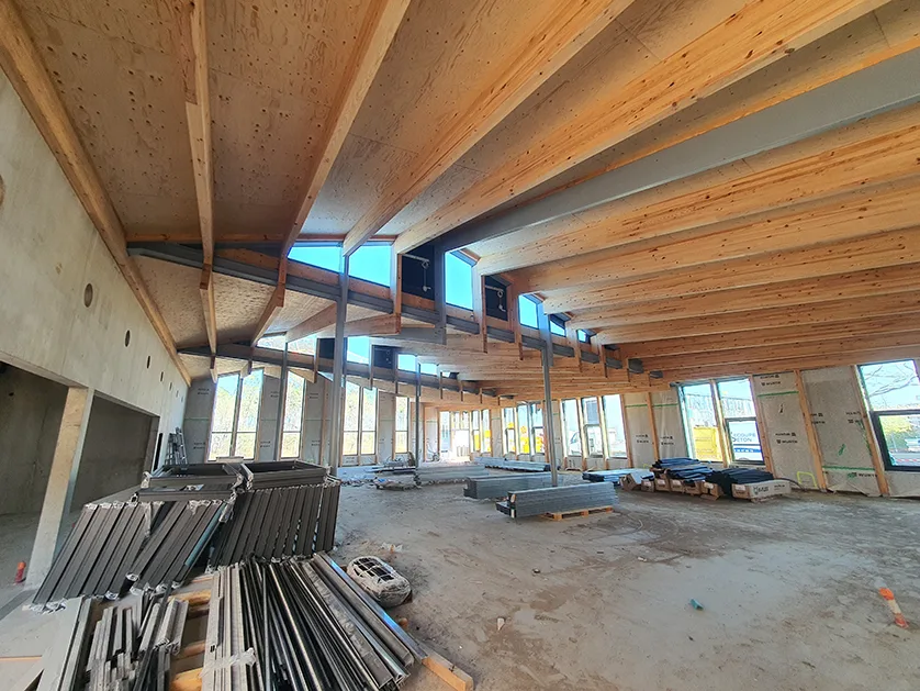 Interior view of a building under construction with exposed wooden beams and concrete walls.