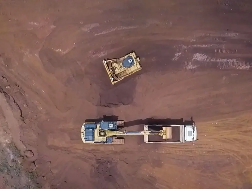 Aerial view of heavy machinery, including an excavator loading a dump truck and a bulldozer, on a construction site.