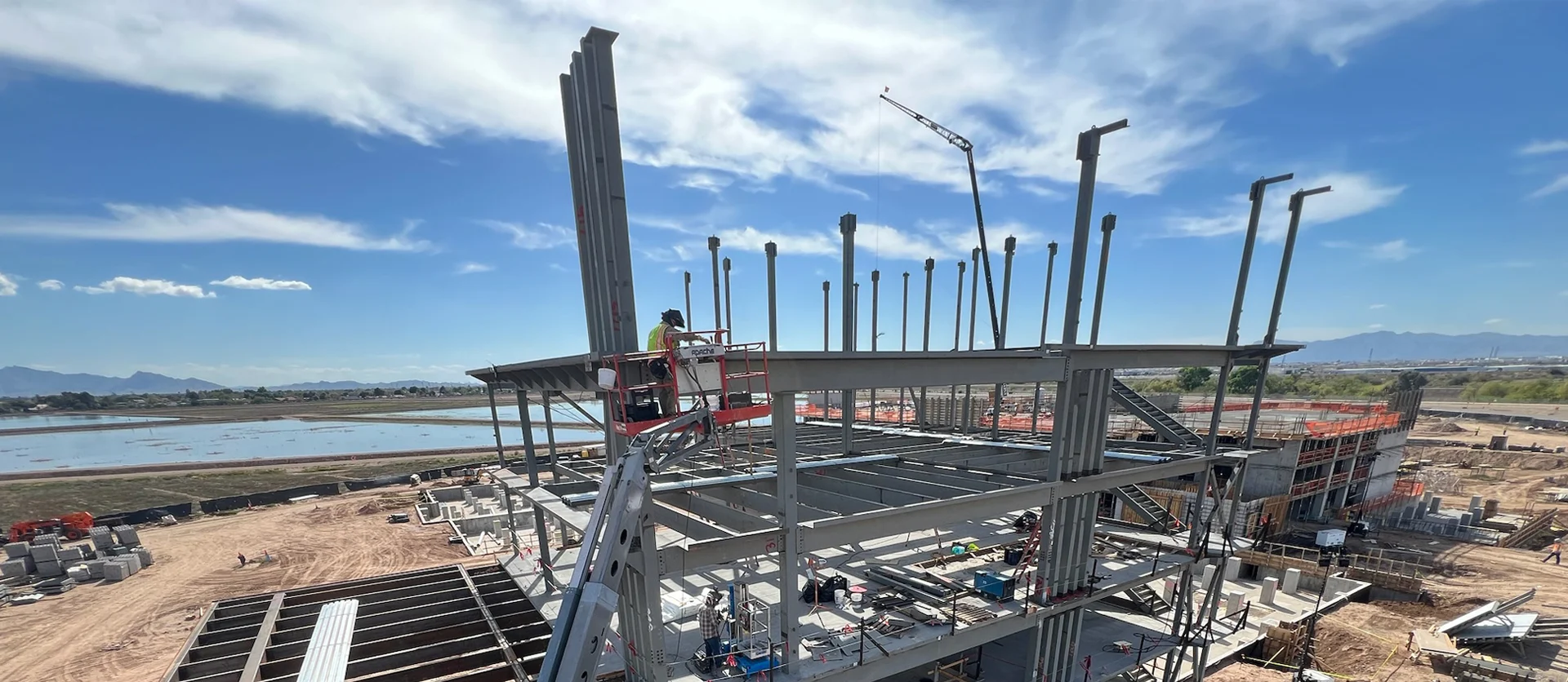 High-angle view of the Fuze ballpark steel frame under construction, with a pickup truck parked below the grid of beams.