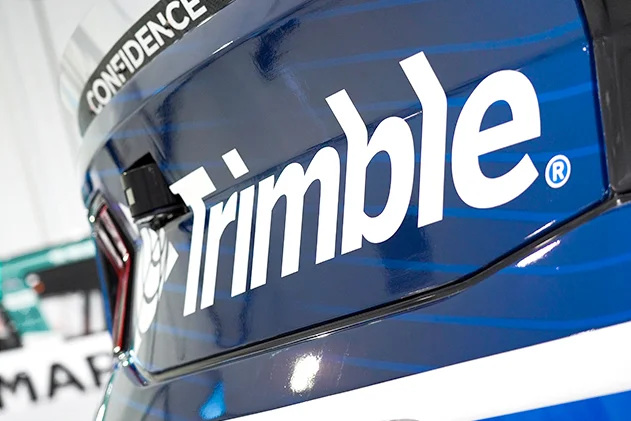 Close-up of a metallic blue vehicle featuring the white Trimble logo and a black banner with the word CONFIDENCE.
