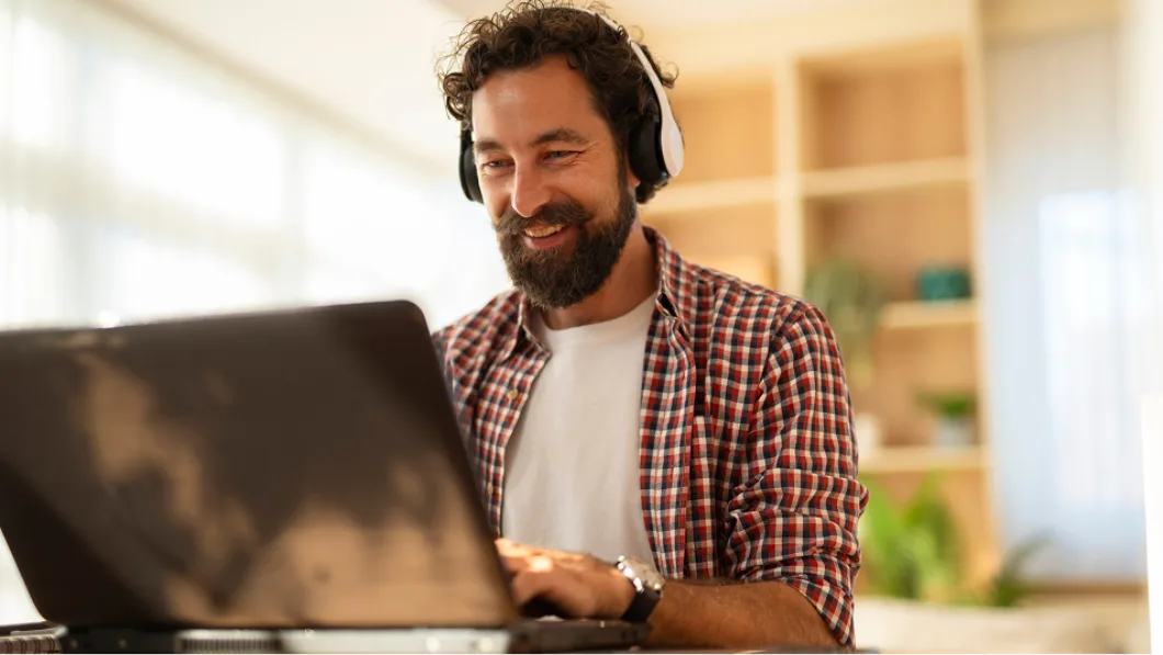 Man wearing headphones working on a laptop in a bright home office