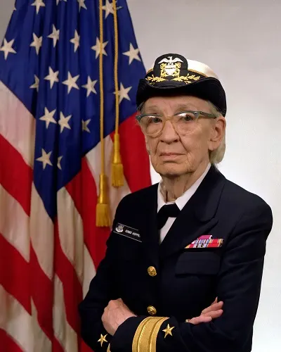 Portrait of a woman in a Navy uniform, standing in front of the American flag.