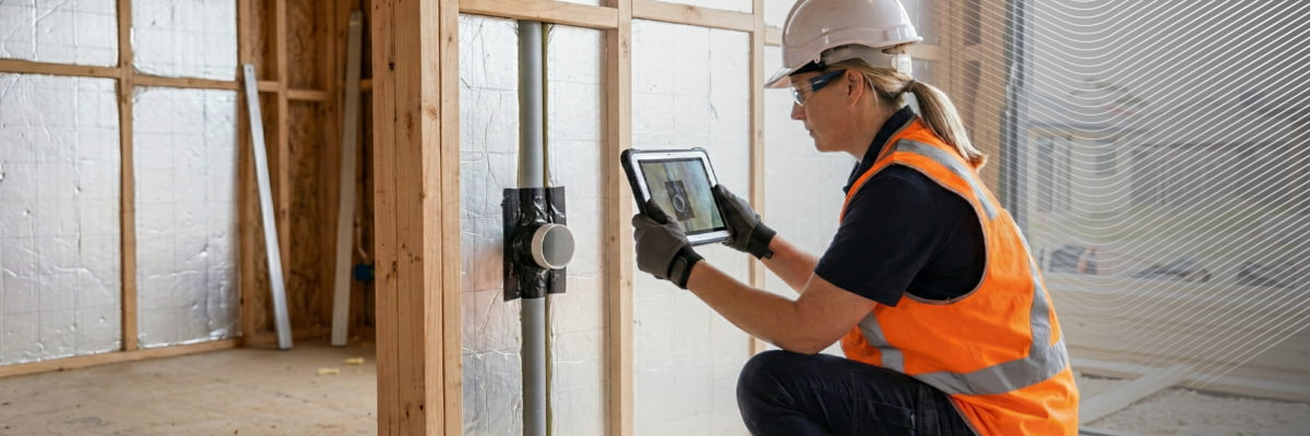 Worker in safety gear using a tablet at a construction site to capture photographic evidence.