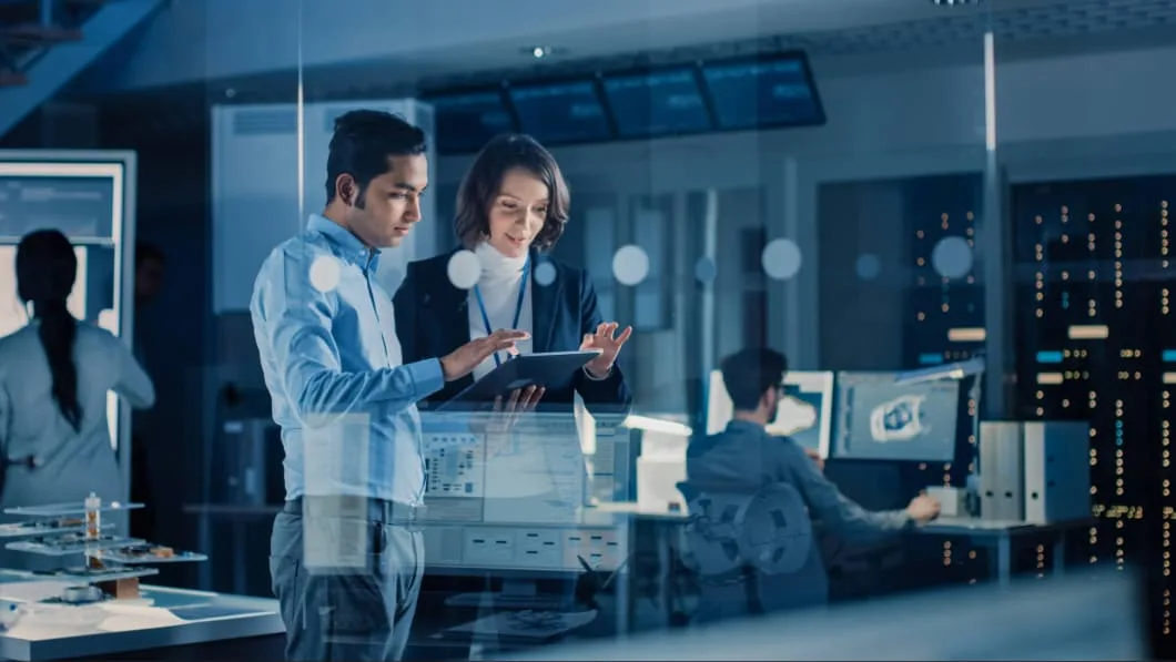 Diverse colleagues collaborating on a digital tablet in a high-tech, blue-lit server room.