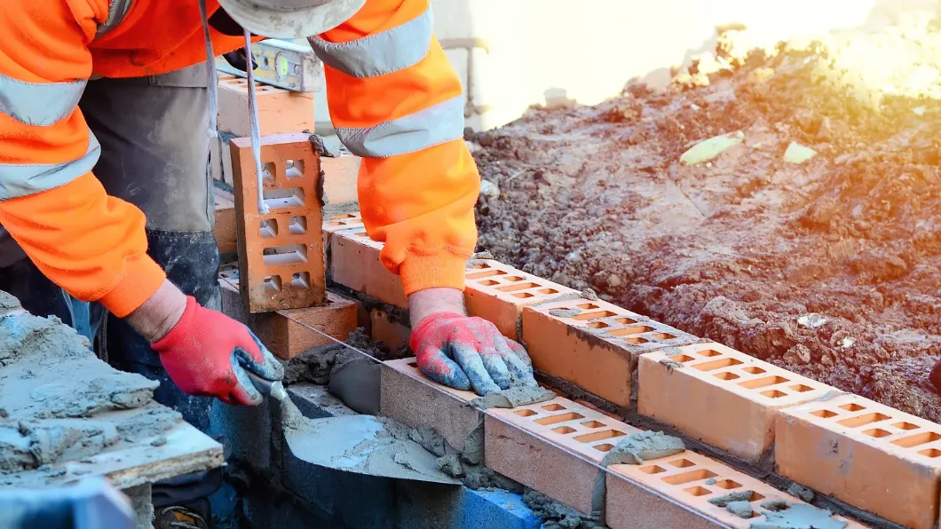 Bricklayer in orange jacket constructing a brick wall with mortar