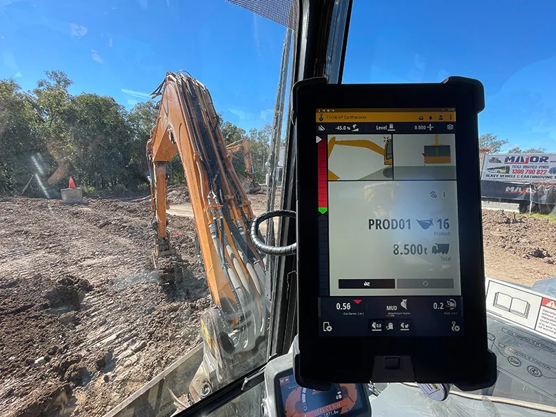 Excavator cab view showing a digital display tracking material movement and two excavators working.