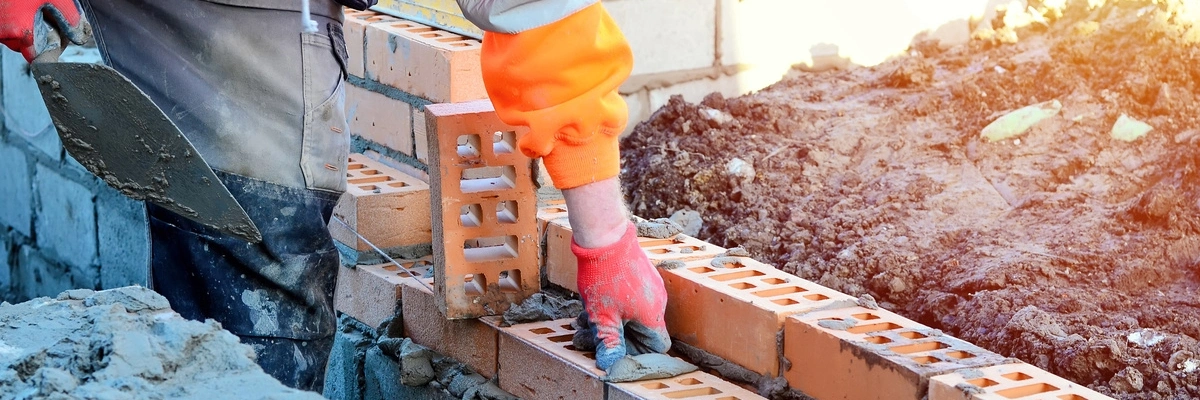 Bricklayer in orange gear laying bricks with mortar on a construction site.