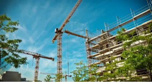 Construction site with cranes and building scaffolding against a blue sky with clouds.