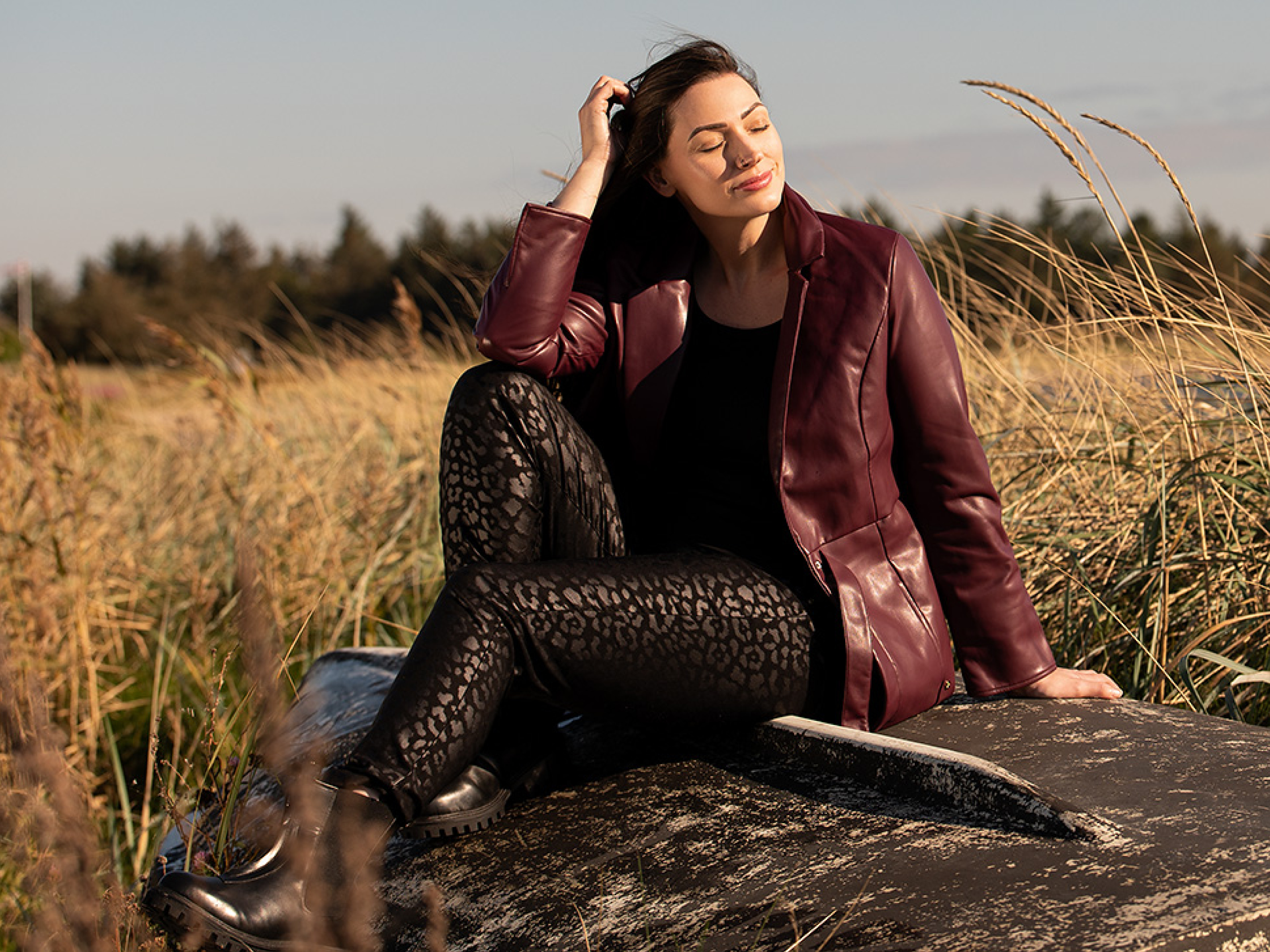 Frau mit burgunderdfarbenem Lederimitatmantel und schwarzer Hose in Glanz-Leoprint