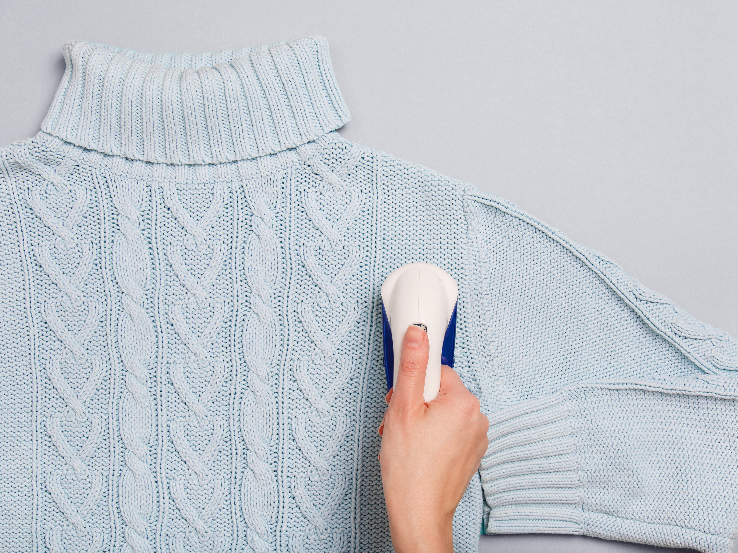 Ein Strickpullover wird mit einem Fusselrasierer gepflegt