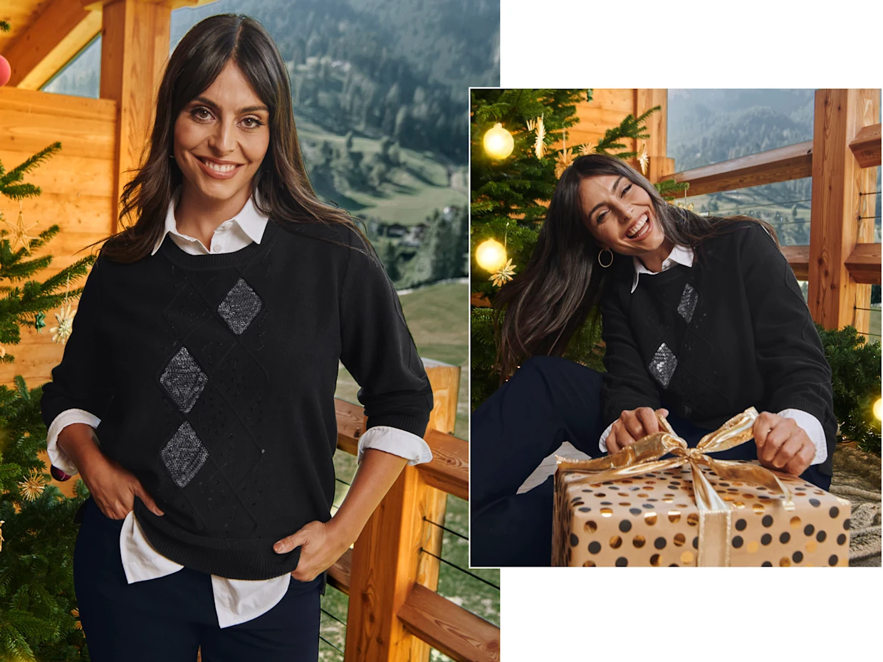 Ein Model in einer weihnachtlich geschmückten Umgebung. Sie trägt einen schwarzen Rauten-Pullover und eine weiße Hemdbluse im Layering-Effekt.