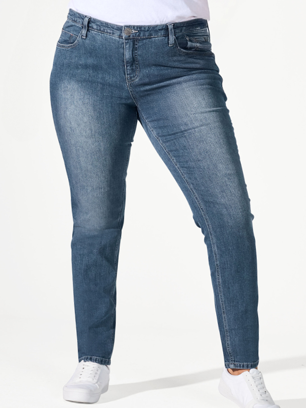 Frau steht in schmaler Jeans vor grauem Hintergrund