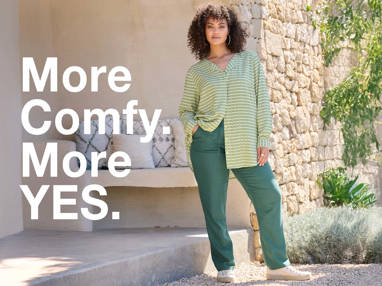 Ein Model in frühlingshafter Outdoor-Umgebung trägt eine mossgrüne Jogg-Pants aus Leinen-Viskose-Mix und eine farblich passende Bluse. Daneben folgender Text: More comfy, more yes.