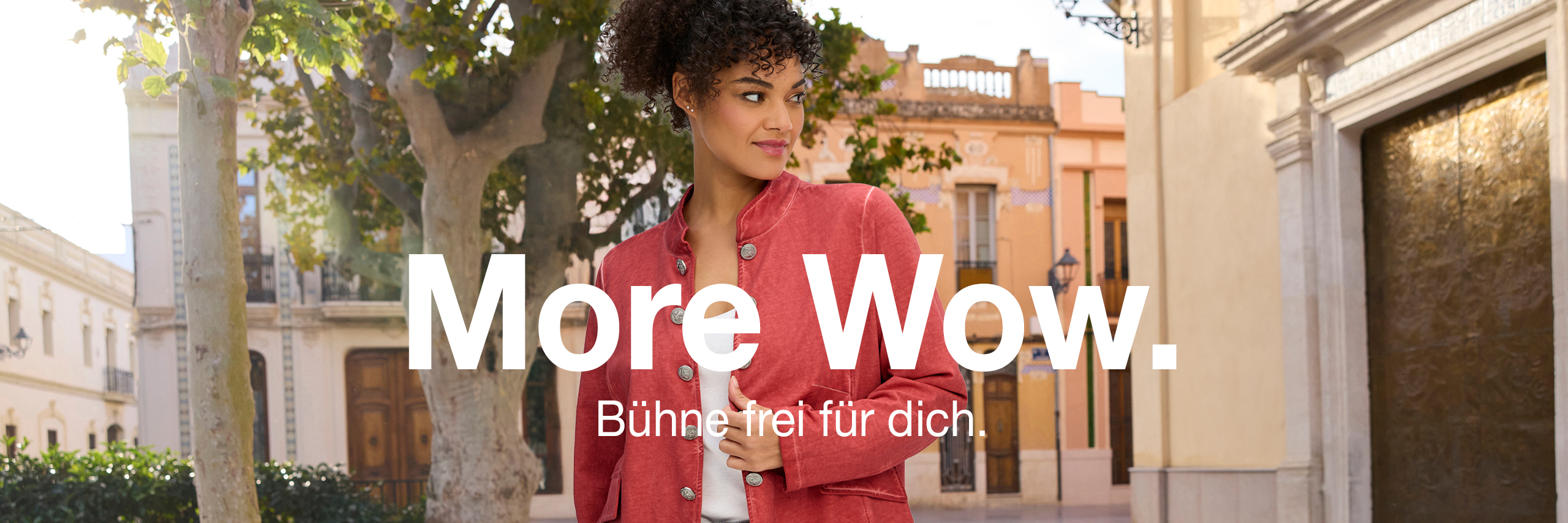 Werbebanner mit Model in rostroter Blazerjacke und Text: More Wow. Bühne frei für dich.