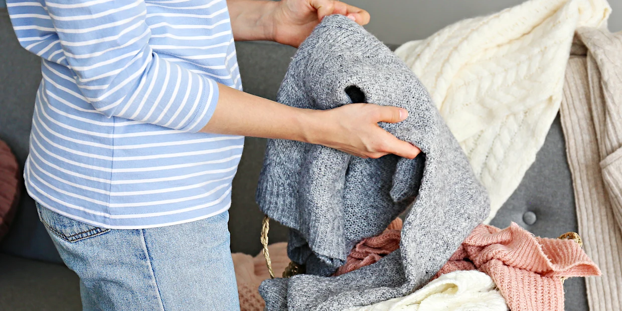 Frau hält einen in der Waschmaschine eingelaufenen Strickpullover in der Hand Frau hält einen in der Waschmaschine eingelaufenen Strickpullover in der Hand