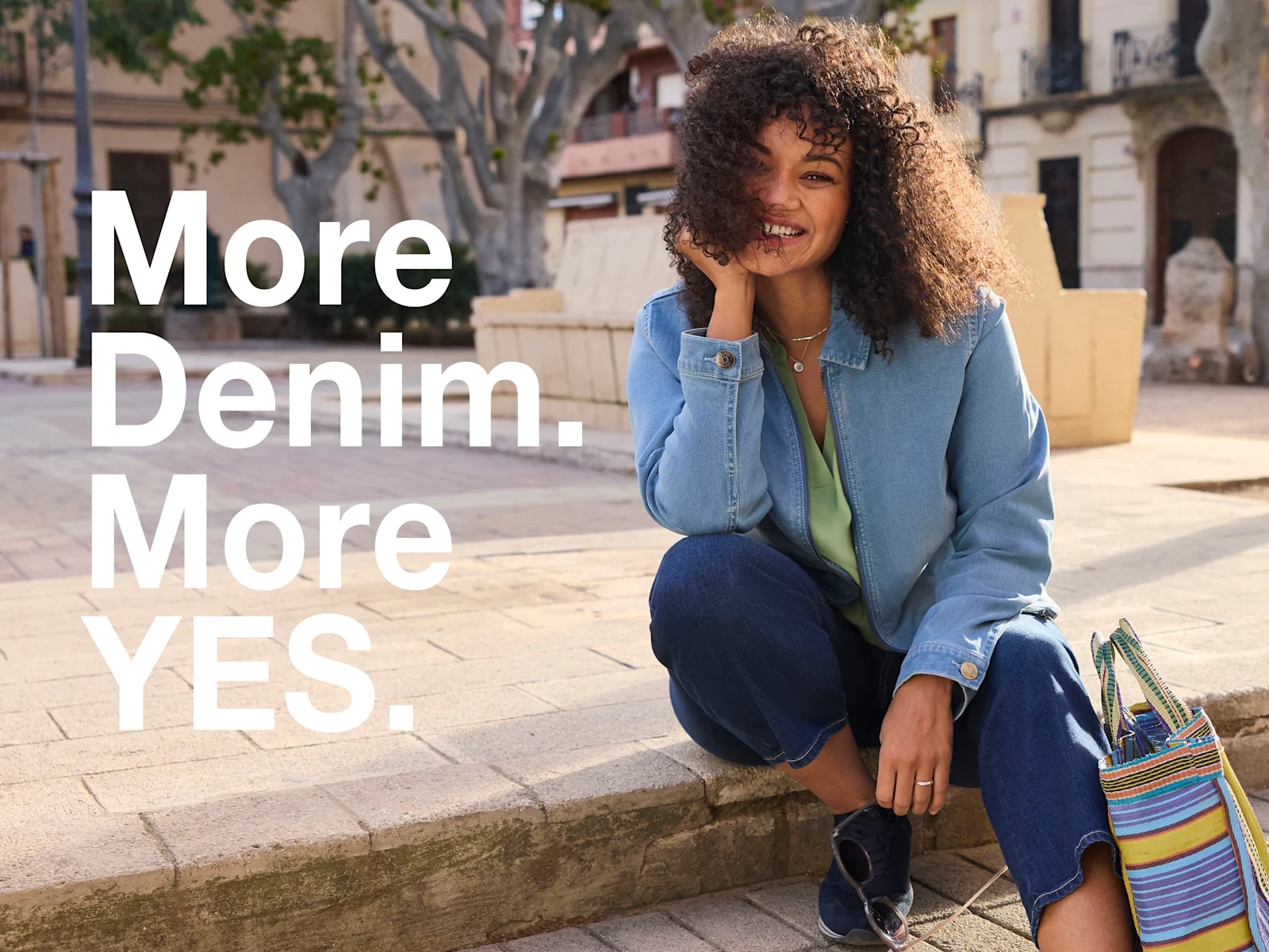 Ein Model in einer frühlingshaften City-Atmosphäre, sie trägt eine eucalyptus-fabene Bluse, eine verkürzt-geschnittenene Jeans in dark blue und eine blue bleached Jeansjacke. Daneben der Text: More Denim, more YES. Ein Model in einer frühlingshaften City-Atmosphäre, sie trägt eine eucalyptus-fabene Bluse, eine verkürzt-geschnittenene Jeans in dark blue und eine blue bleached Jeansjacke. Daneben der Text: More Denim, more YES.
