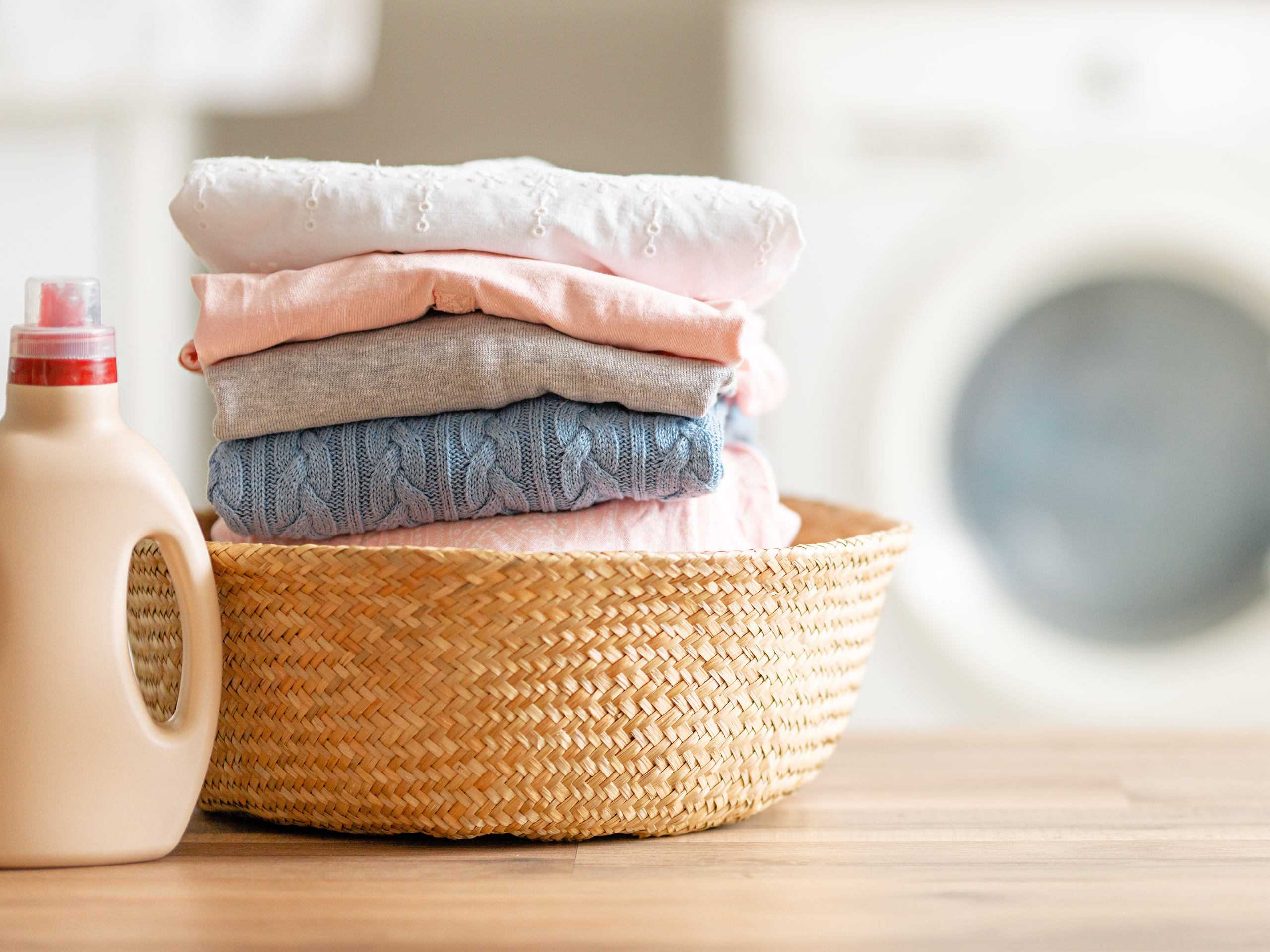Waschmittelbehälter mit einem Stapel an Kleidung. Im Hintergrund ist eine Waschmaschine