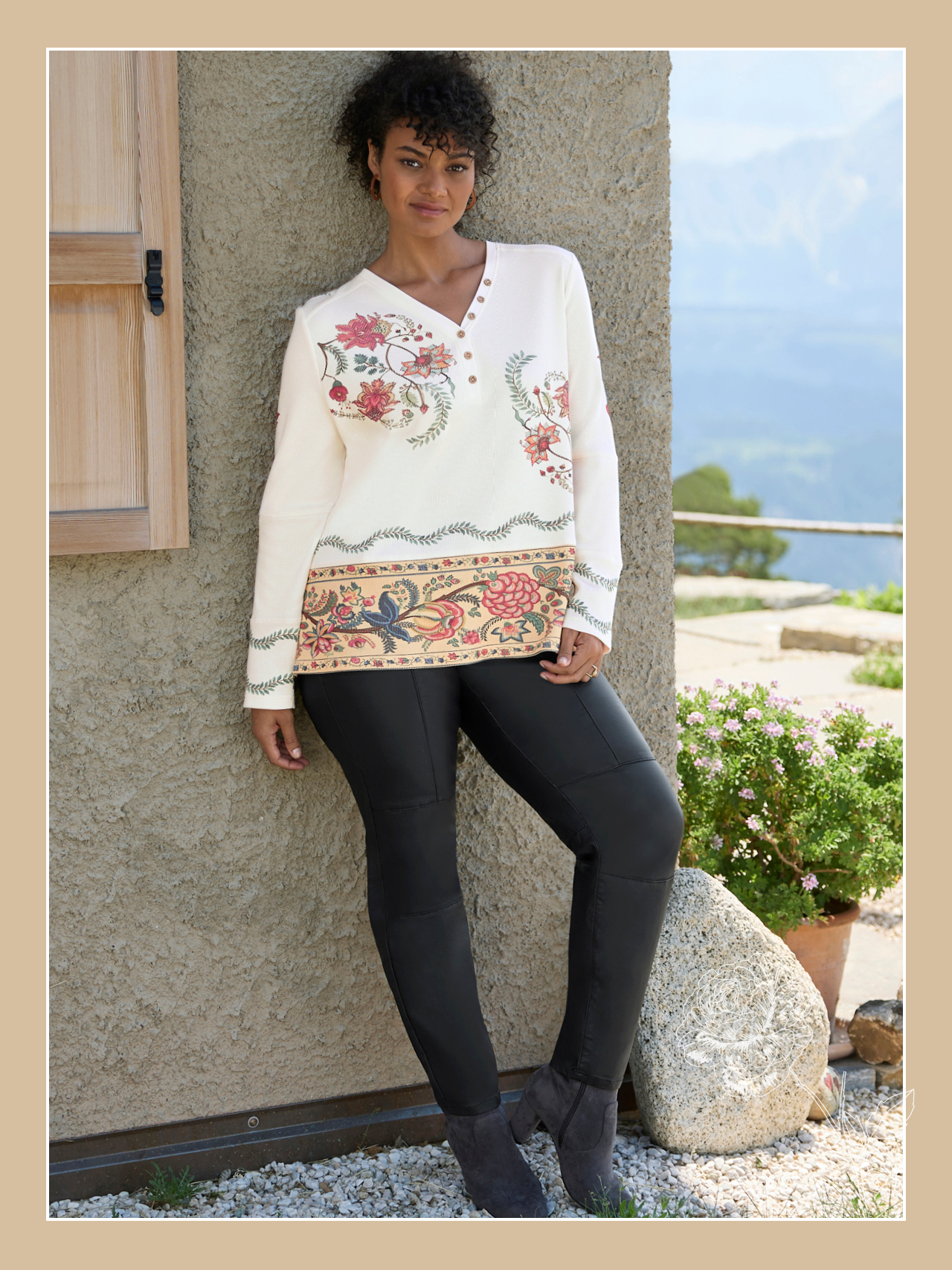 Ein Model trägt ein champagner-rostrot-bedrucktes Langarmshirt mit floralem Muster und eine schwarze Hose