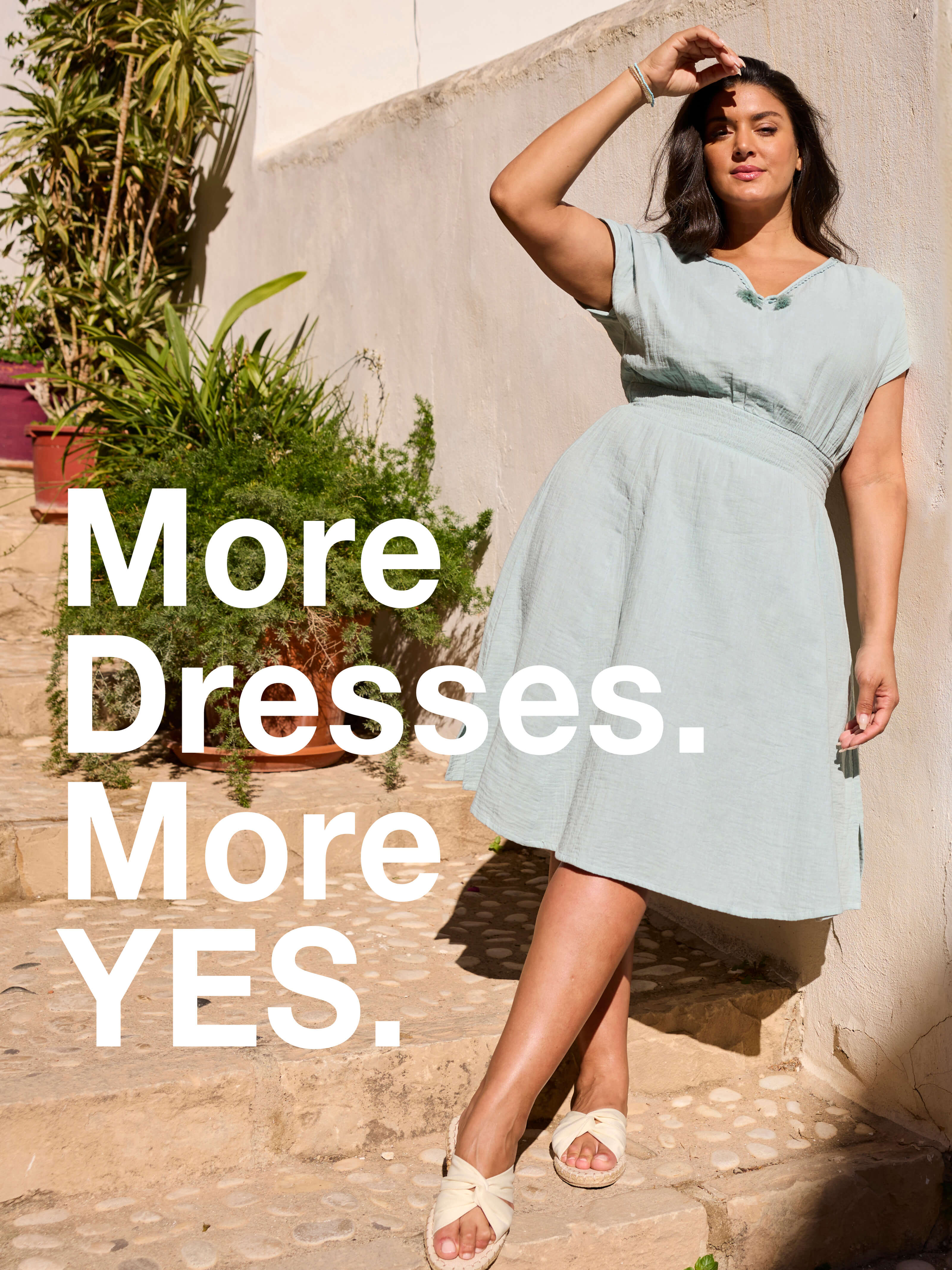 Ein Model in frühlingshafter Outdoor-Umgebung trägt ein kalkmint-farbenes Sommerkleid  aus Musselin. Daneben folgender Text: More dresses, more yes.