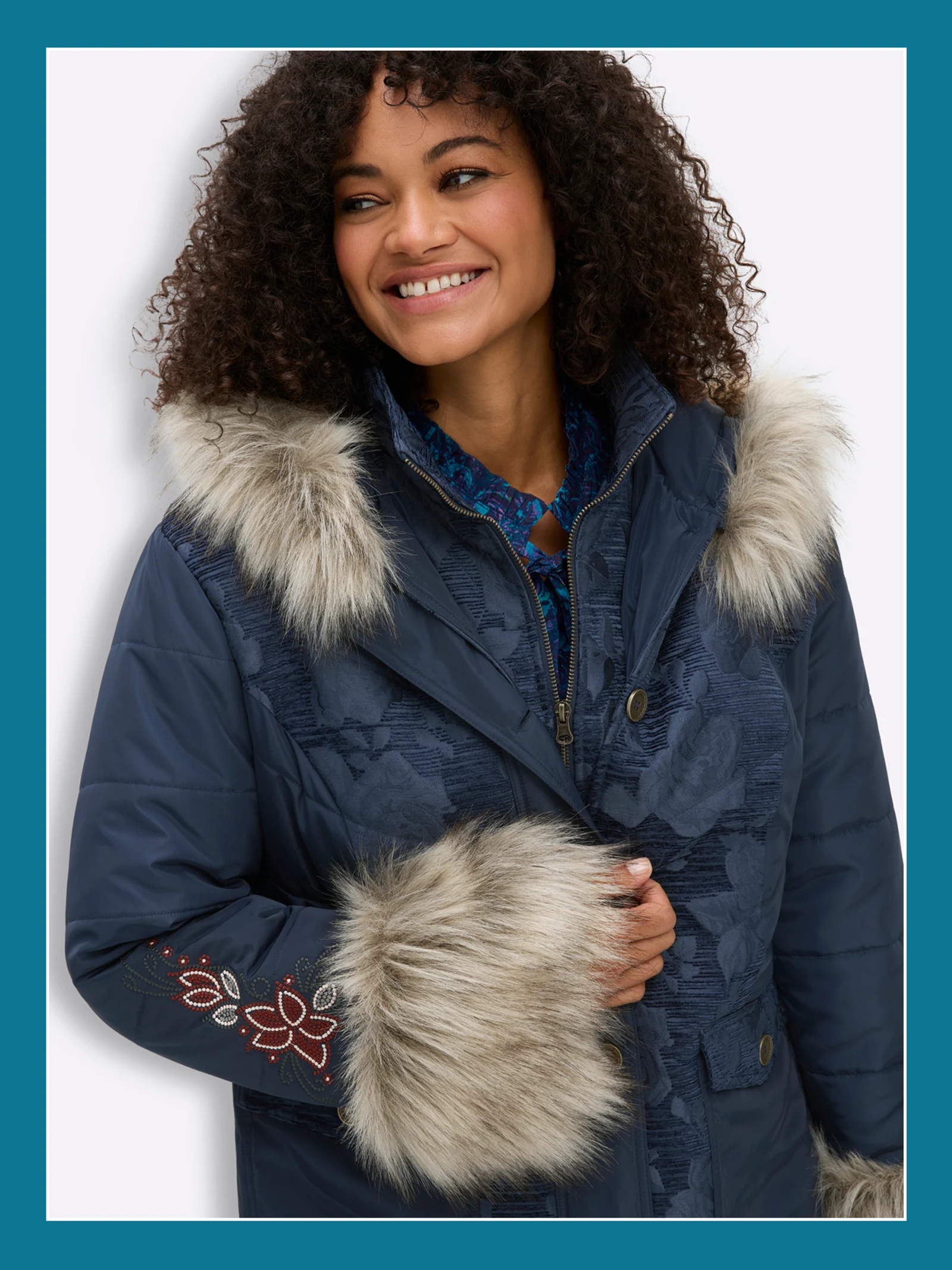 Ein Model trägt eine dunkelblaue Winterjacke mit Jacquardmuster, Blumenstickereien und Fell-Imitat.
