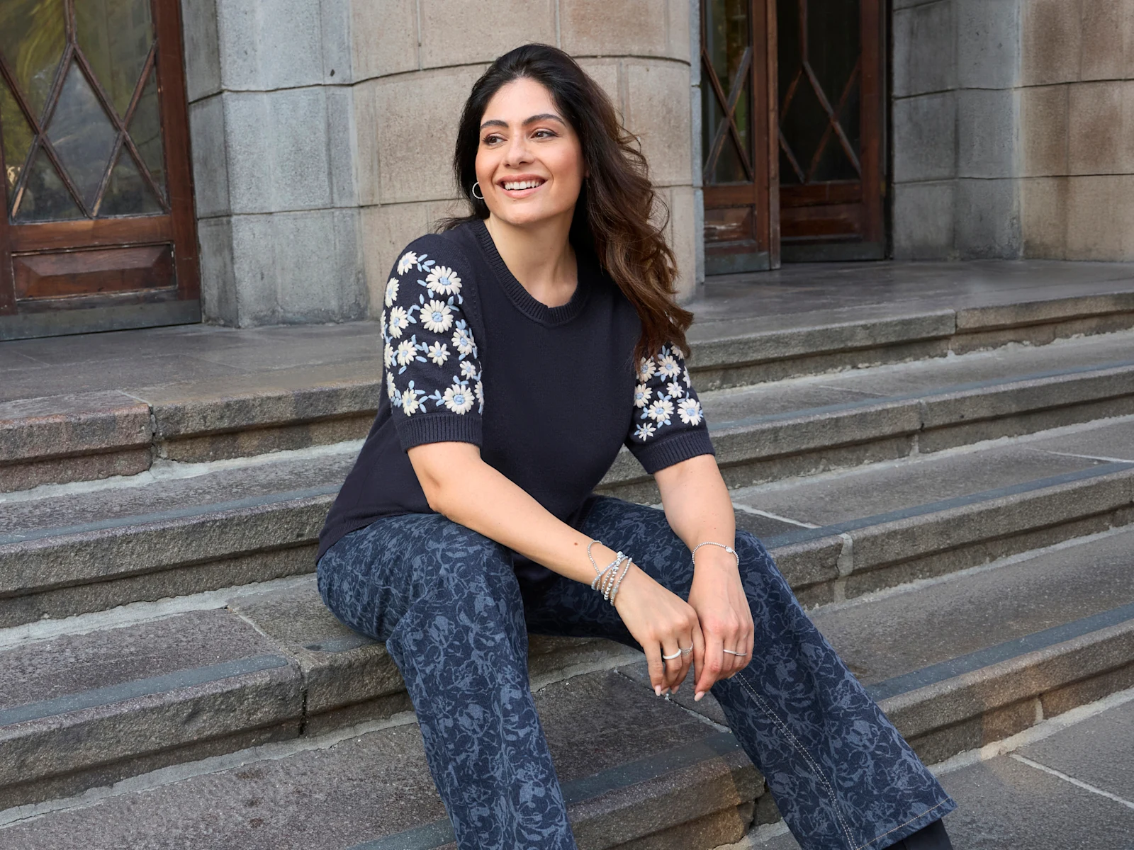 Ein Model trägt einen tiefblau-ecru farbenen Pullover mit weißen Blütenstickereien am Ärmel und eine dark blue-gemustert Jeans mit weitem Bein. Ein Model trägt einen tiefblau-ecru farbenen Pullover mit weißen Blütenstickereien am Ärmel und eine dark blue-gemustert Jeans mit weitem Bein.