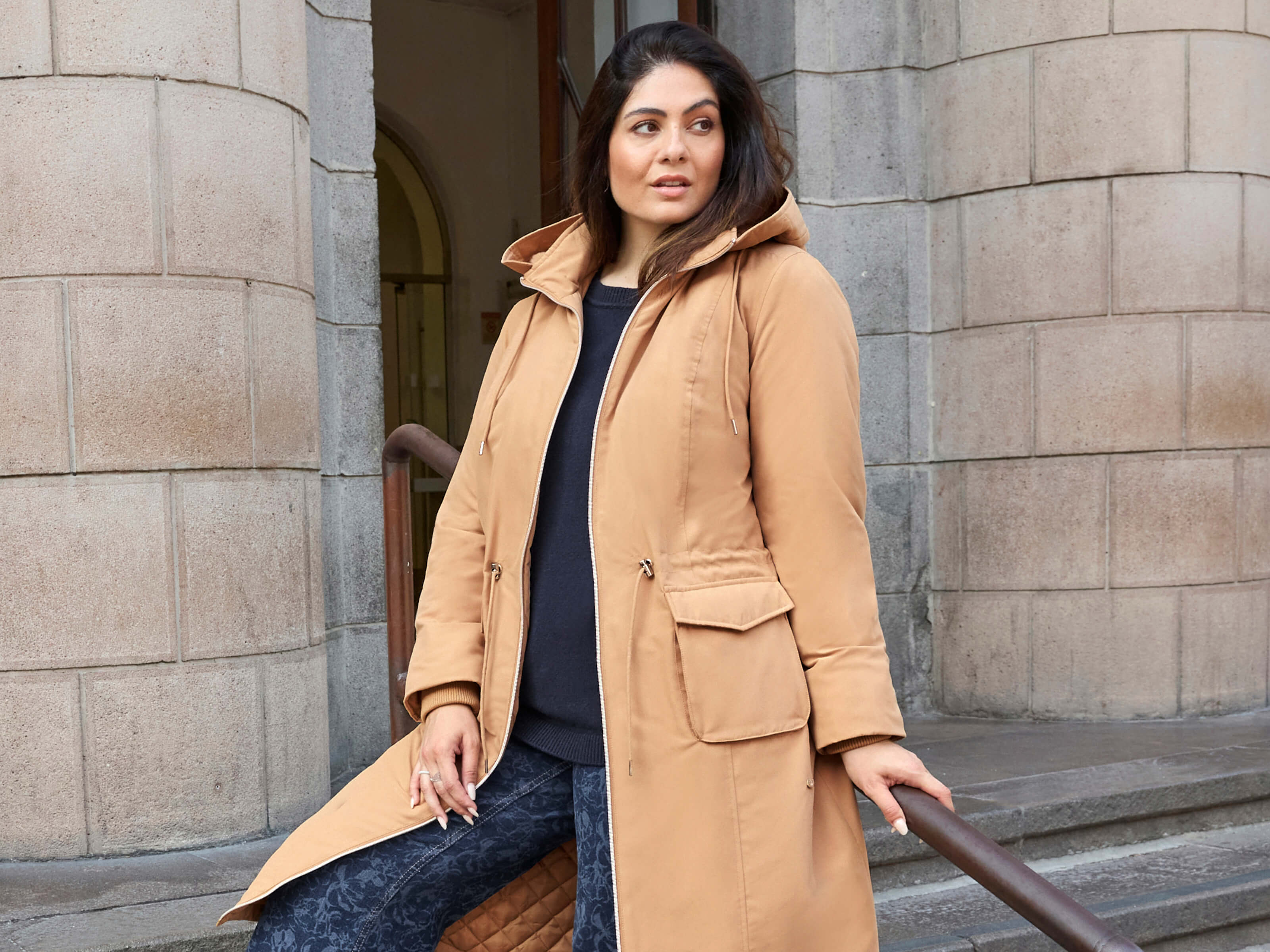 Ein Model trägt einen camel farbenen Parka in wärmender Qualität und einen blauen Pullover