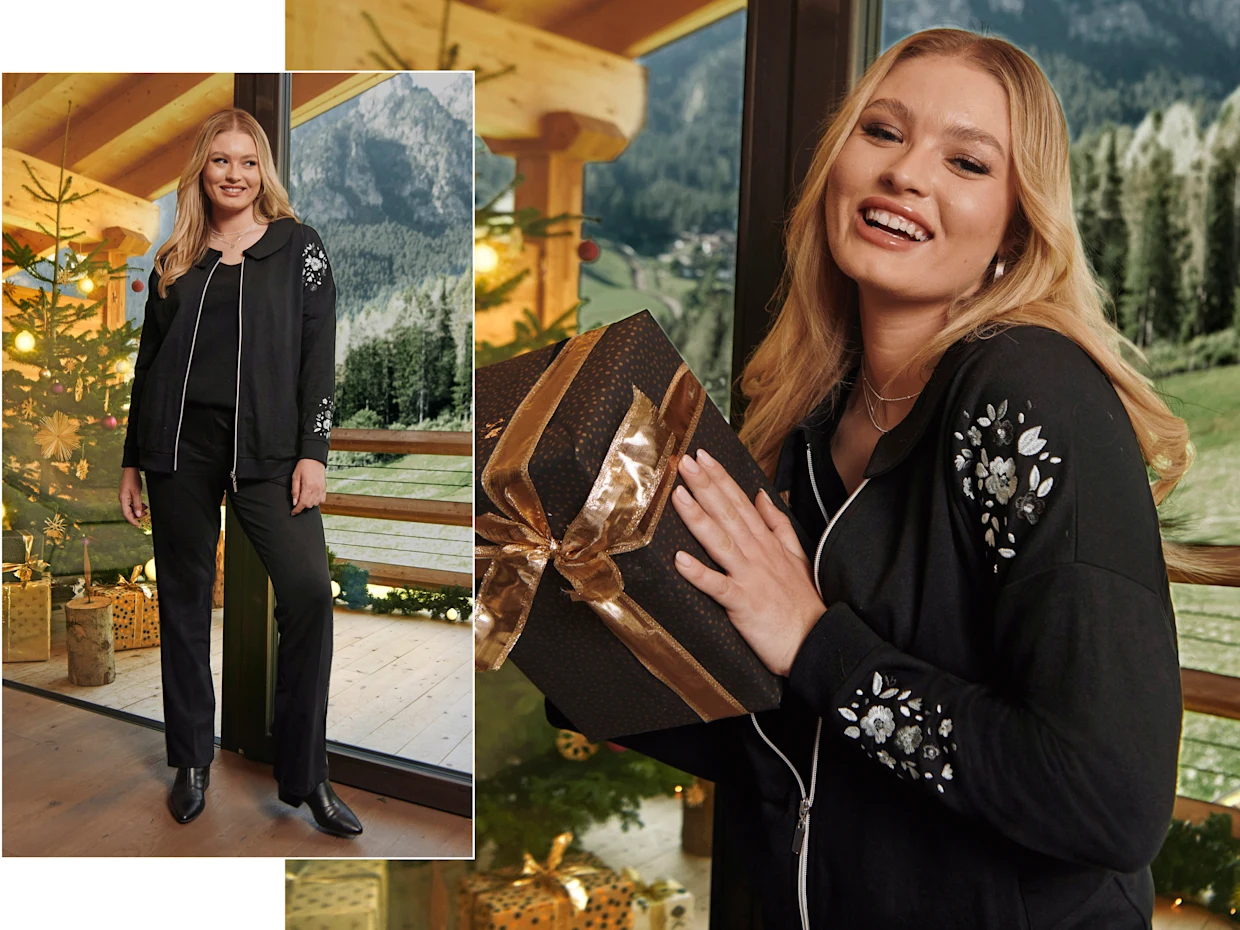 Ein Model in einer weihnachtlich geschmückten Umgebung. Sie trägt eine schwarze Sweatjacke mit Pailletten-Blüten und eine schwarze Bootcut-Jeans mit silberfarbenen Paspeln.