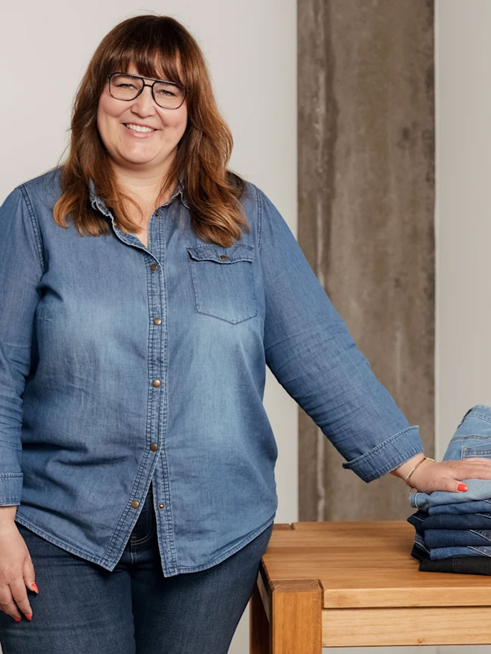 Frau steht am Tisch und legt Hand auf einen Stapel mit Jeans