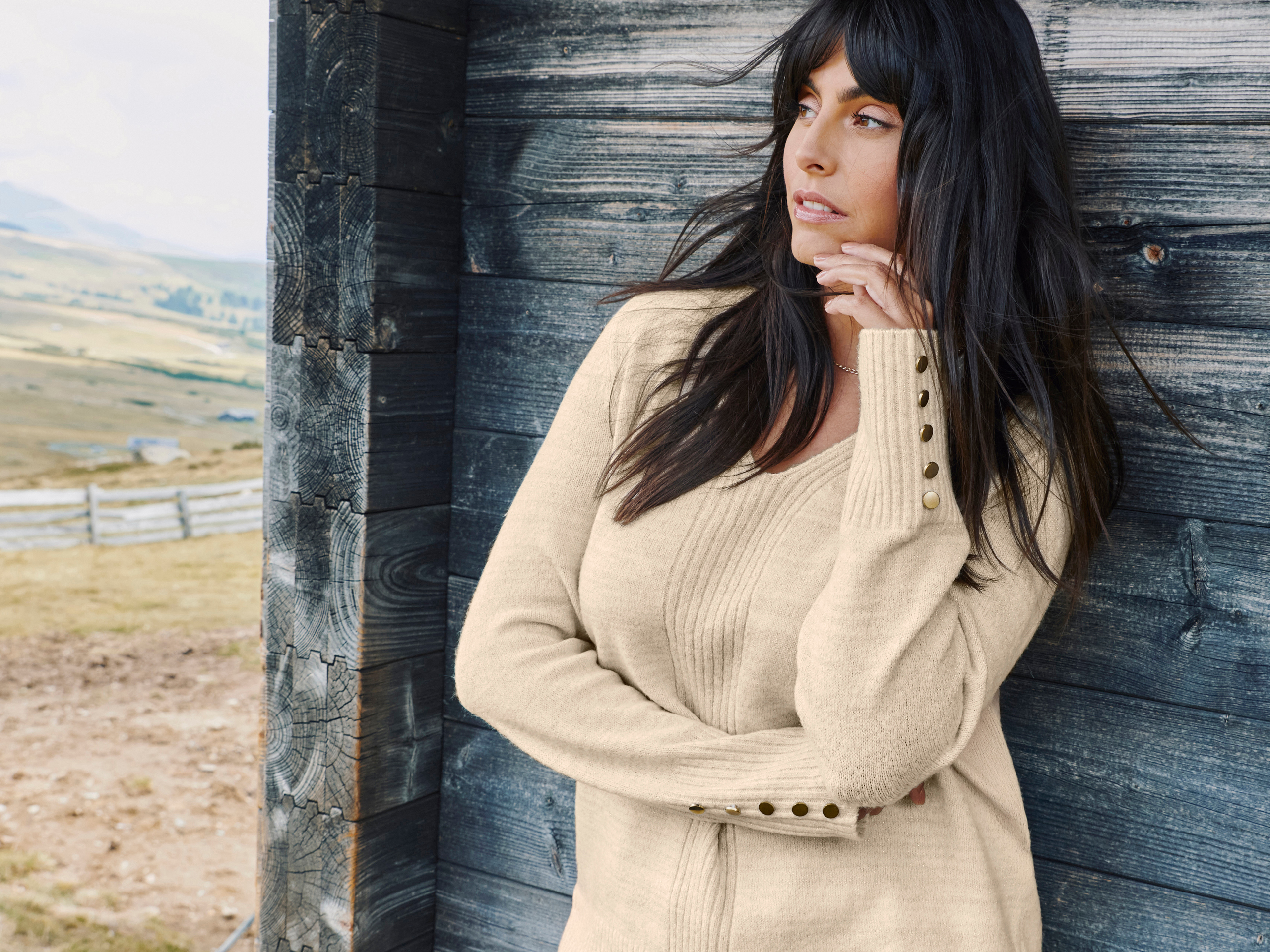 Model in sandfarbenem Pullover mit Zierknöpfen an den Ärmeln
