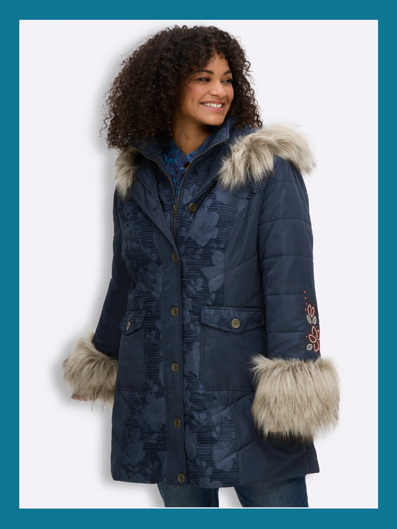 Ein Model trägt eine dunkelblaue Winterjacke mit Jacquardmuster, Blumenstickereien und Fell-Imitat.