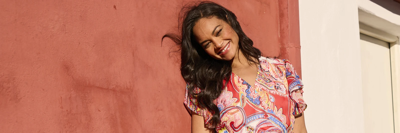 Frau lehnt mit einem sommerlichen Oberteil an einer Terracottafarbenen Wand Frau lehnt mit einem sommerlichen Oberteil an einer Terracottafarbenen Wand