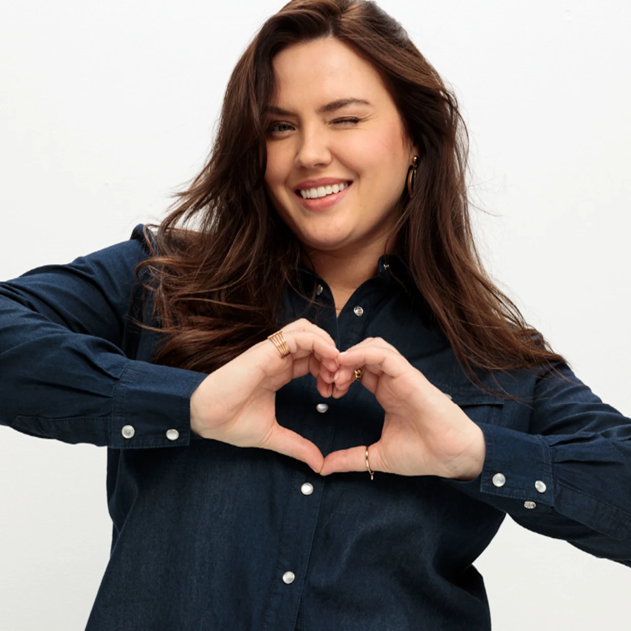 Frau im Jeanshemd zeigt Herz vor hellem Hintergrund Frau im Jeanshemd zeigt Herz vor hellem Hintergrund