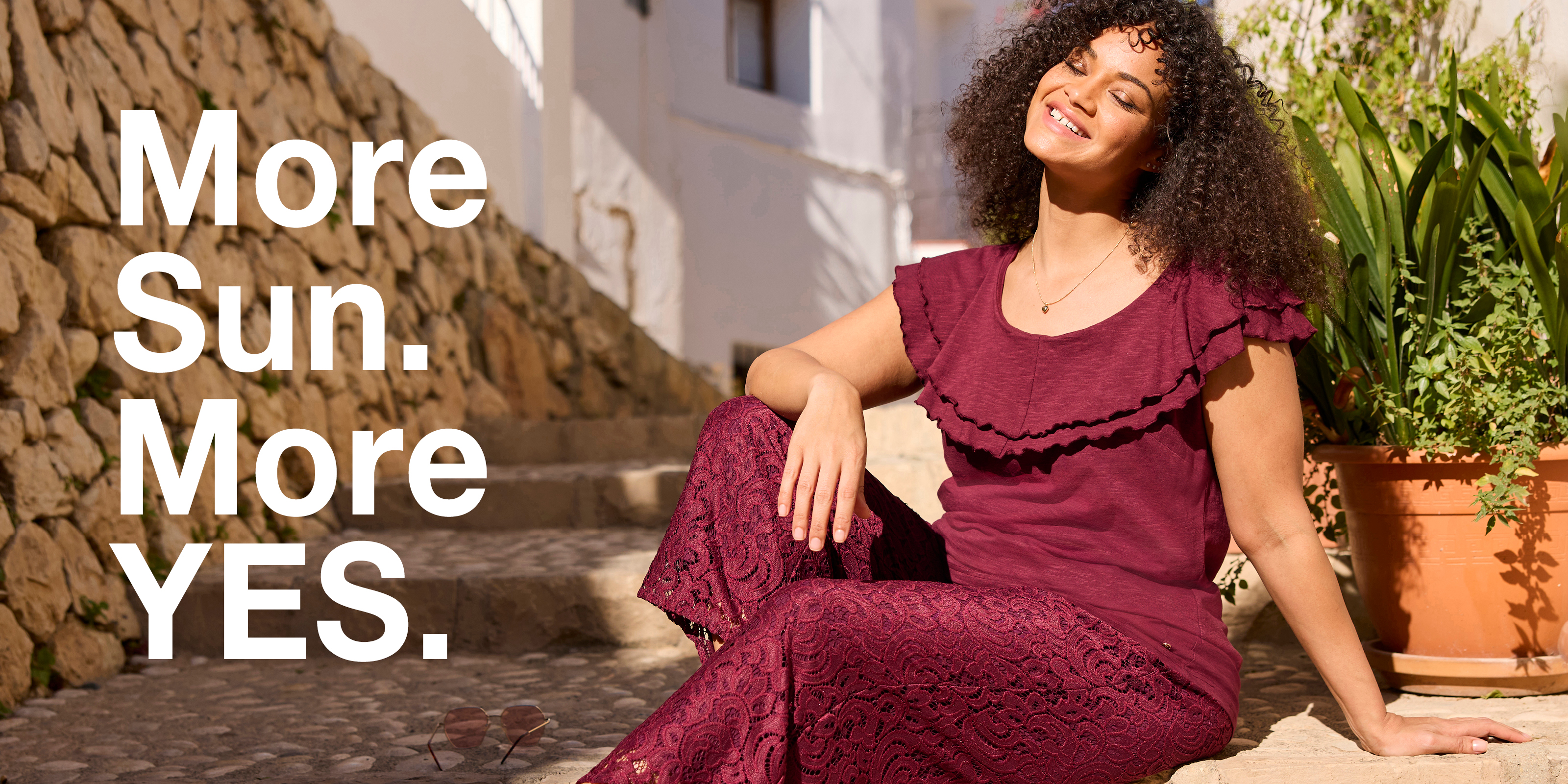 Werbebanner mit Model in bordeauxrotem Shirt und gleichfarbiger Hose mit Spitzenmuster und Text: More Sun. More YES.