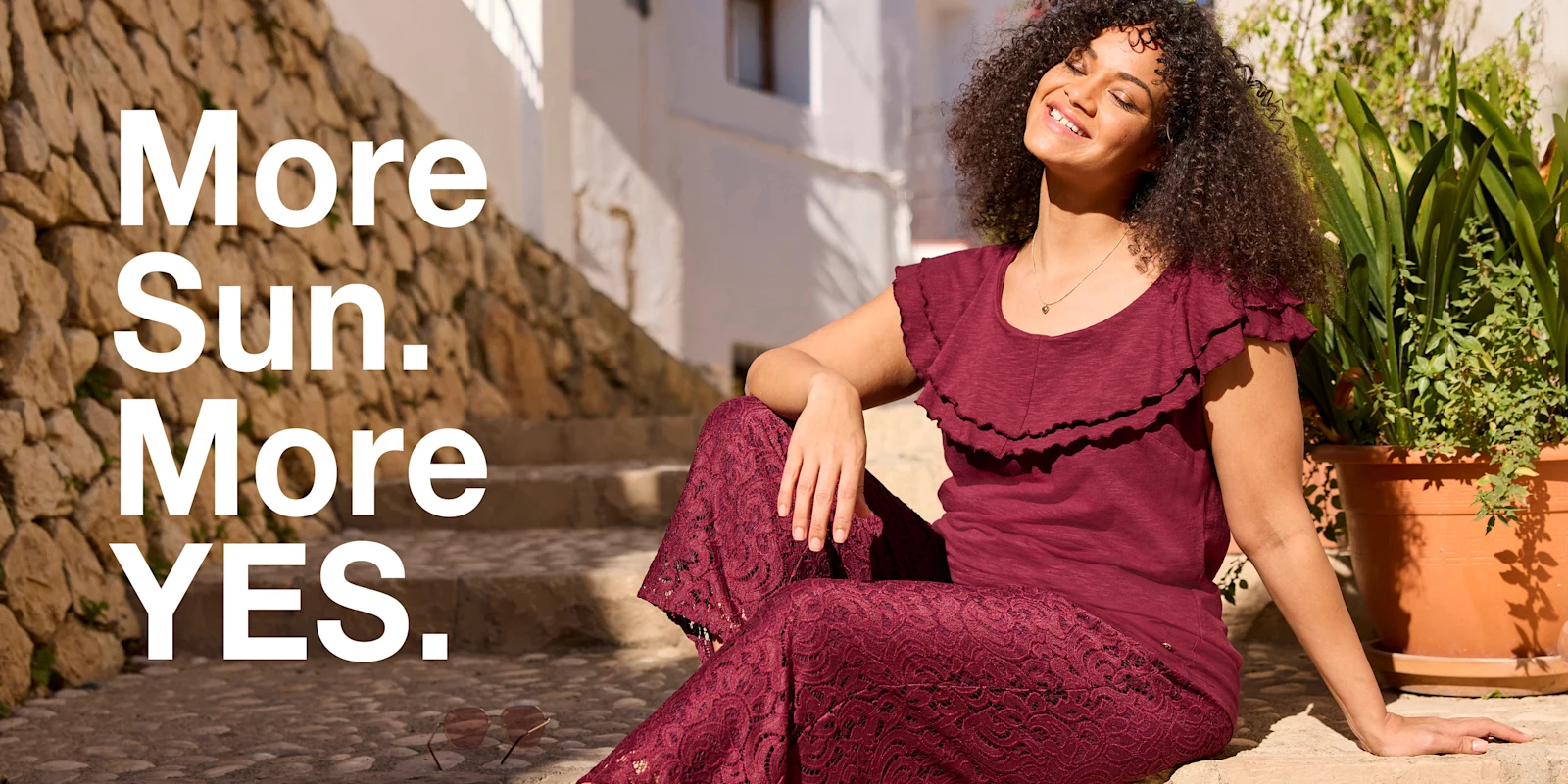 Werbebanner mit Model in bordeauxrotem Shirt und gleichfarbiger Hose mit Spitzenmuster und Text: More Sun. More YES.