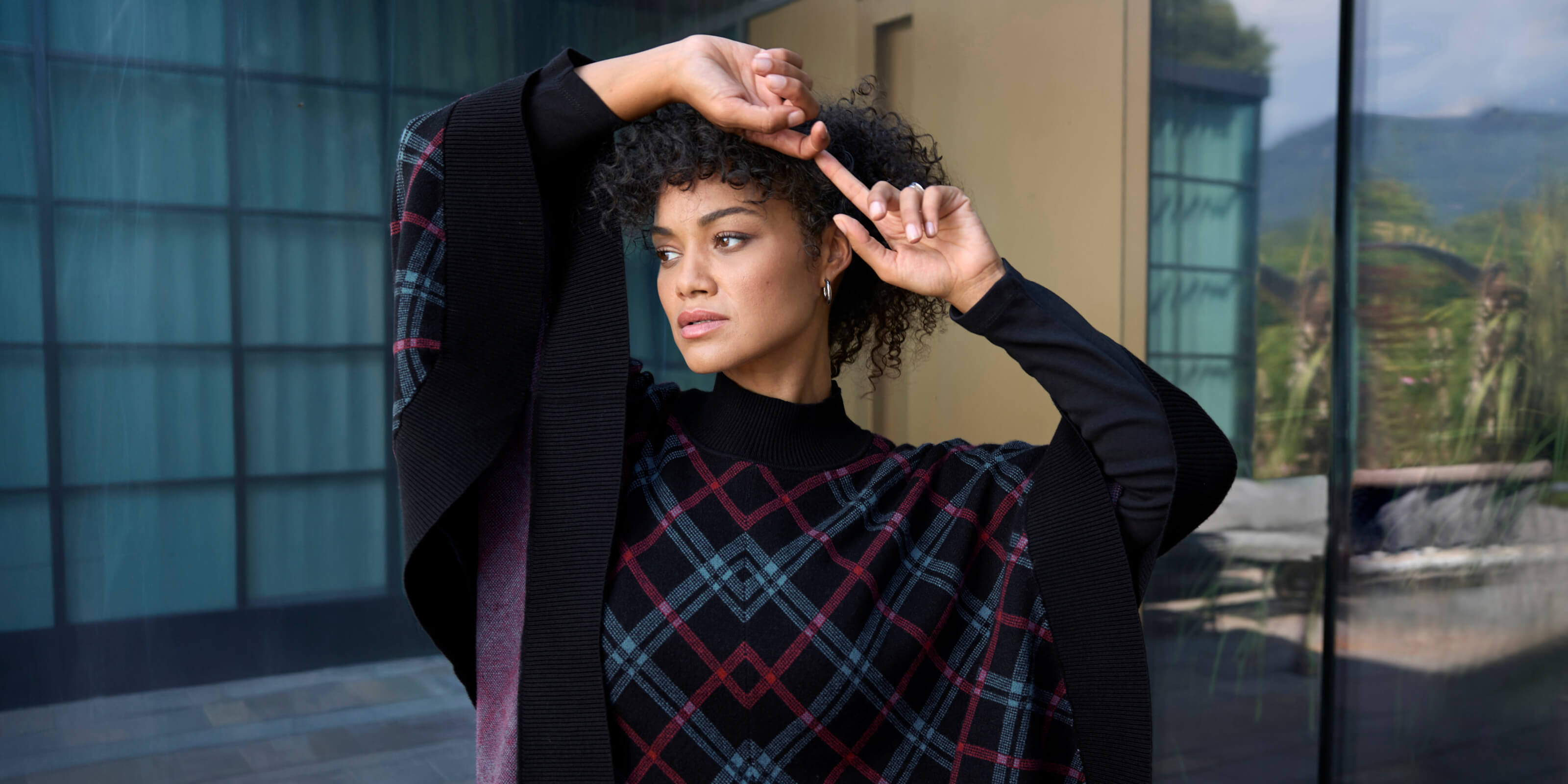 Ein Model trägt einen schwarz-bordeaux-karierten Strickponcho mit Karomuster. Daneben folgender Text:  Bereit für den Winter. Die neue Kollektion ist da