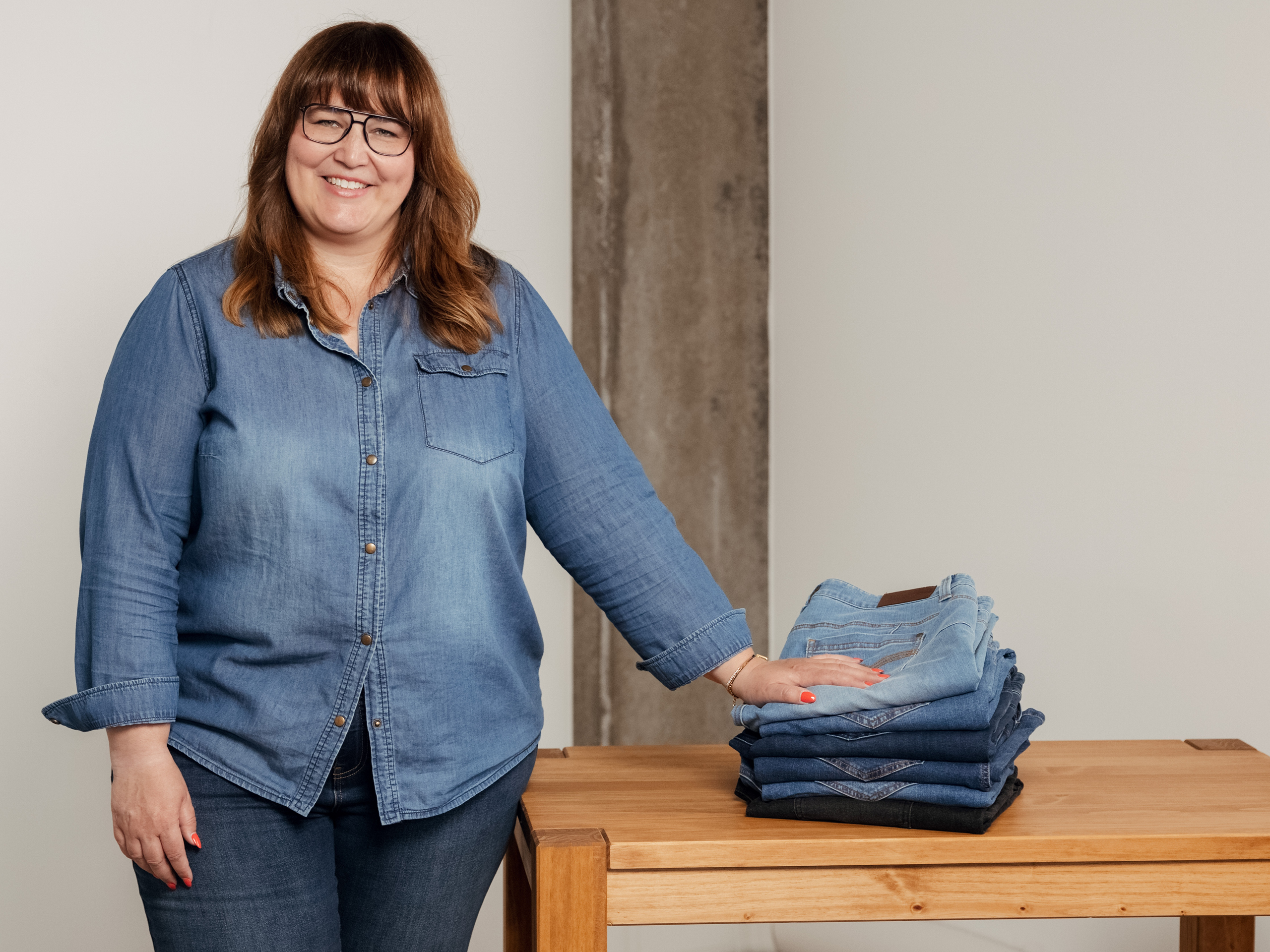 Frau im Jeanshemd steht an einem Tisch und legt ihre Hand auf einen Stapel mit Jeanshosen