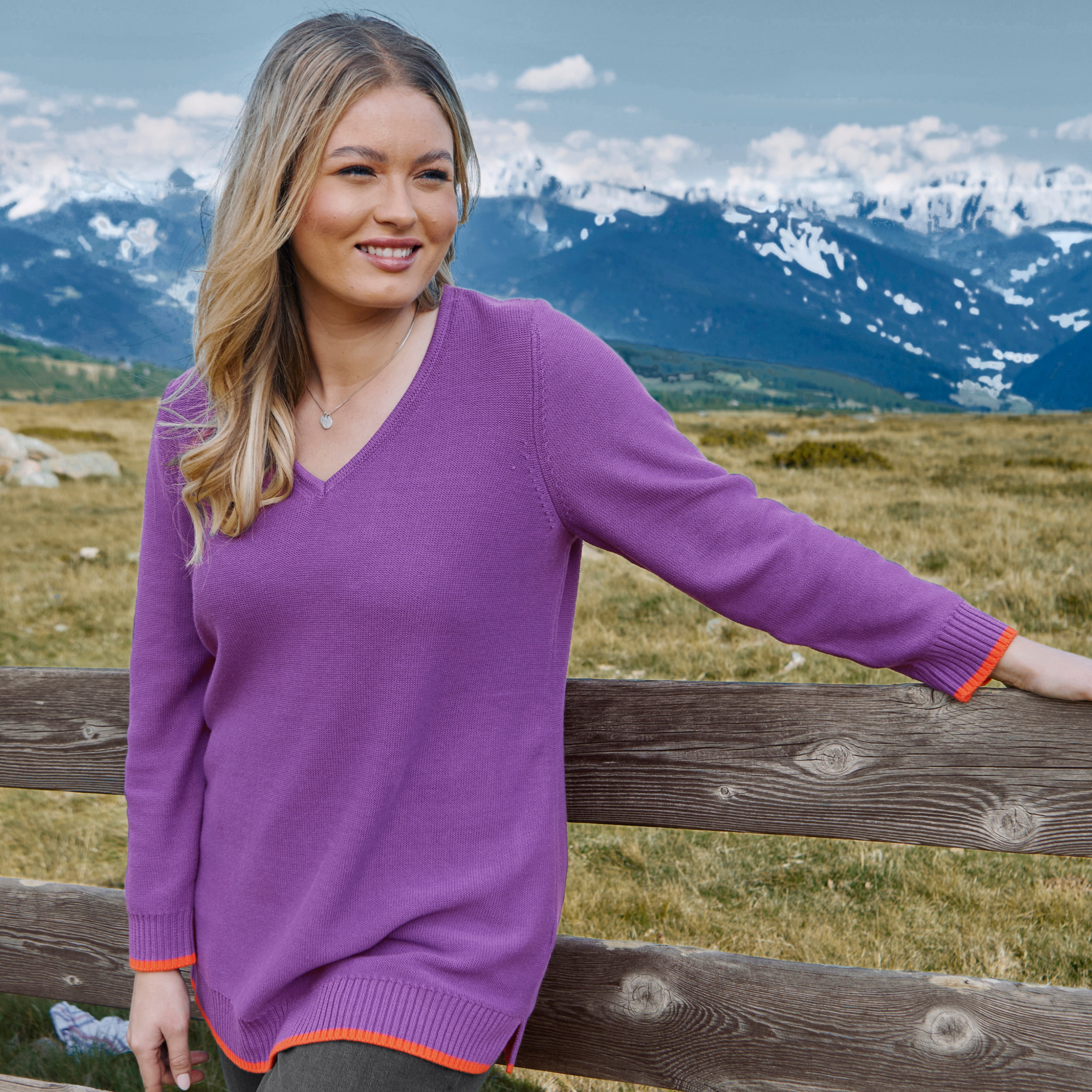 Model in lila Pullover mit orangefarbenen Bündchen