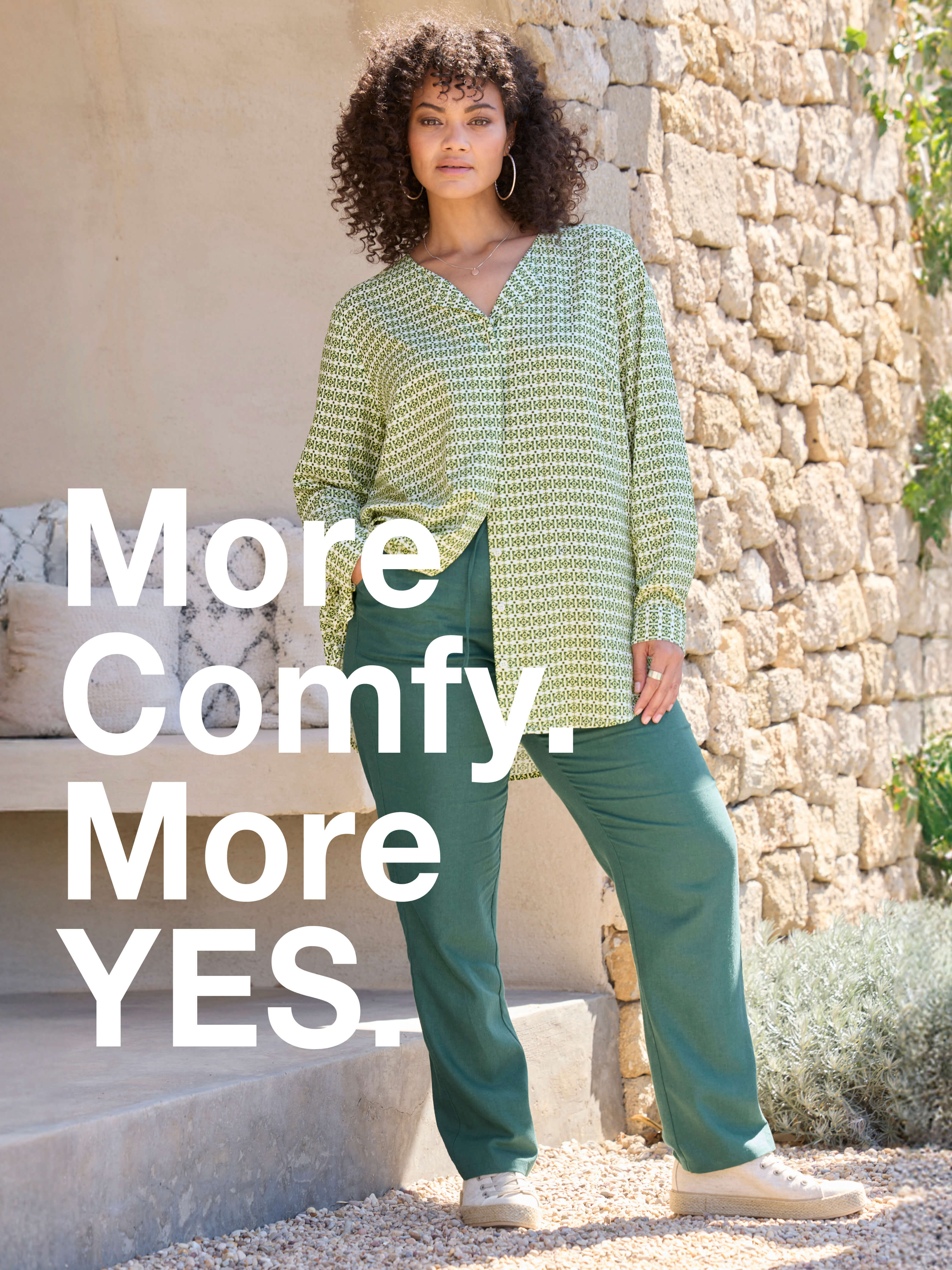 Ein Model in frühlingshafter Outdoor-Umgebung trägt eine  mossgrüne Jogg-Pants aus Leinen-Viskose-Mix und eine farblich passende Bluse.  Daneben folgender Text: More comfy, more yes.